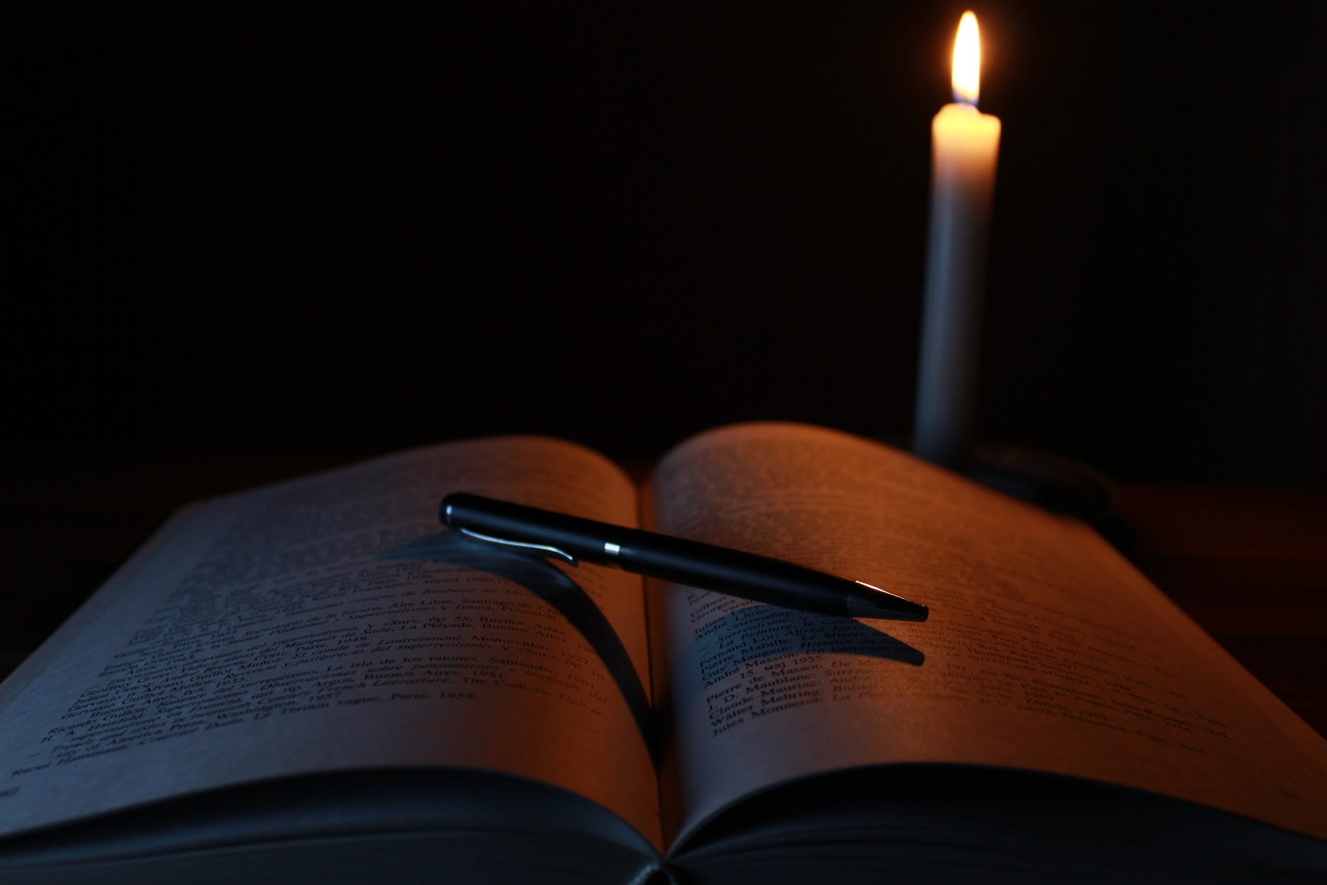 black pen on opened book beside lit taper candle
