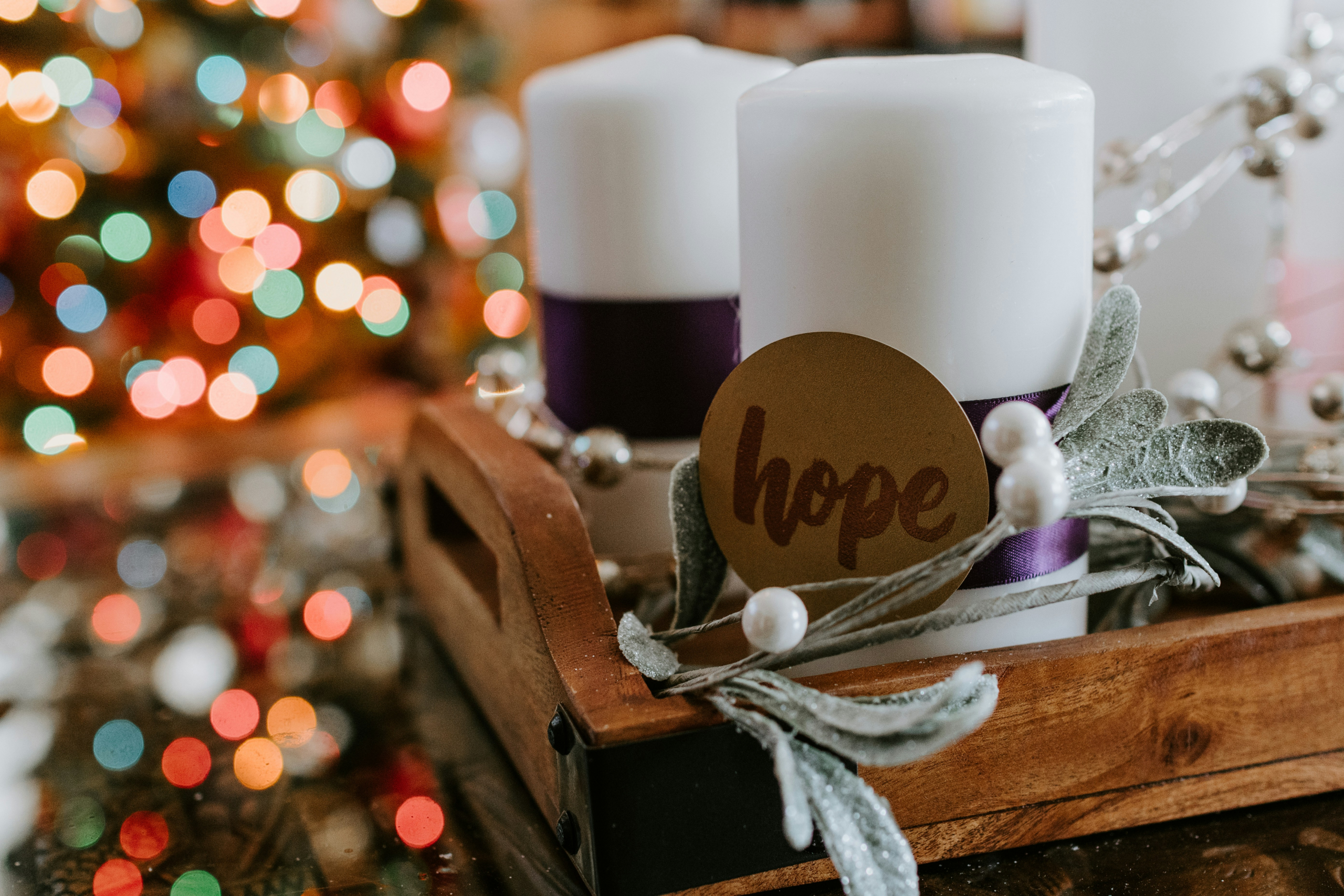 White candles next to a multi-colored lit Christmas tree. One candle has a label that says Hope.